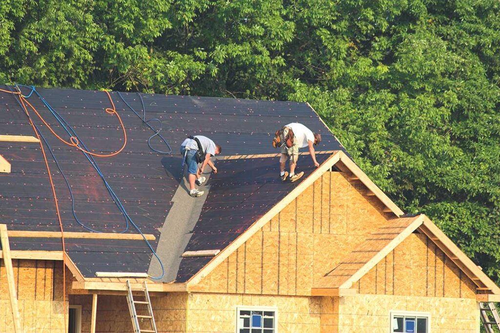 A person using a tape measure and level to check the slope of a shingle roof on a residential house.