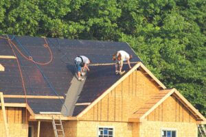 A person using a tape measure and level to check the slope of a shingle roof on a residential house.