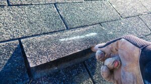Close view of layered metal flashing around a chimney where shingles meet a roof surface.